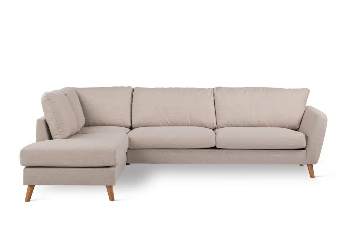 Een beige L-vormige sectionele bank met zachte zittingen en rugleuningen. Het heeft houten poten en een chaise longue aan de linkerkant, wat een moderne en gezellige zitopstelling creëert. De bank staat tegen een witte achtergrond.