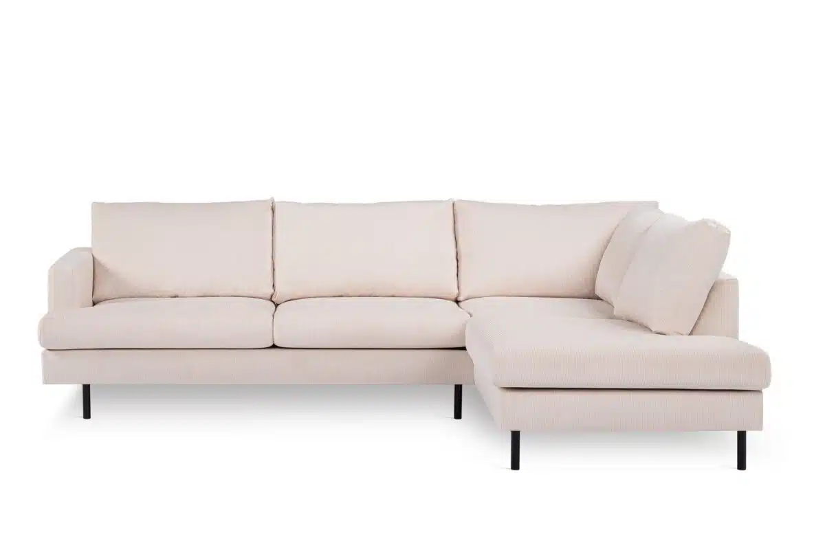 Een lichtbeige L-vormige sectionele bank met drie gestoffeerde zittingen aan de linkerkant en een chaise longue aan de rechterkant. Het heeft zwarte, slanke poten en een minimalistisch ontwerp, tegen een effen witte achtergrond.