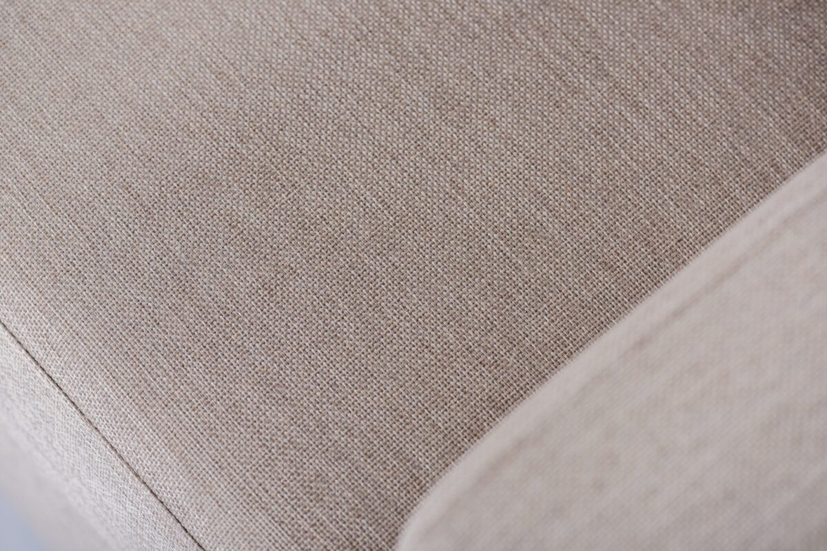 Close-up van een beige stoffen hoekbank, met de geweven textuur. De afbeelding benadrukt het gladde oppervlak van de stof en subtiele kleurvariaties, waardoor de bekledingsdetails worden benadrukt.