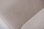Close-up van een beige stoffen hoekbank, met de geweven textuur. De afbeelding benadrukt het gladde oppervlak van de stof en subtiele kleurvariaties, waardoor de bekledingsdetails worden benadrukt.