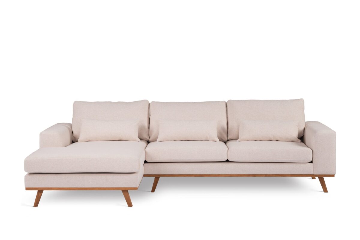 Een moderne beige sectionele bank met houten poten. De bank heeft drie zitkussens en een loungegedeelte aan de linkerkant, waardoor een ruime en comfortabele zithoek ontstaat.