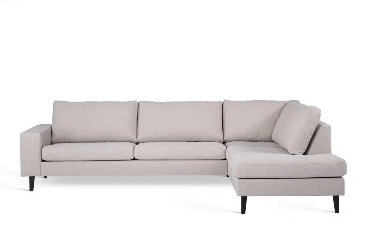 Een moderne L-vormige sectionele bank met lichtgrijze bekleding en zwarte metalen poten. Het ontwerp is minimalistisch, met drie rugkussens aan de lange kant en een chaise longue aan de rechterkant. De achtergrond is effen wit.