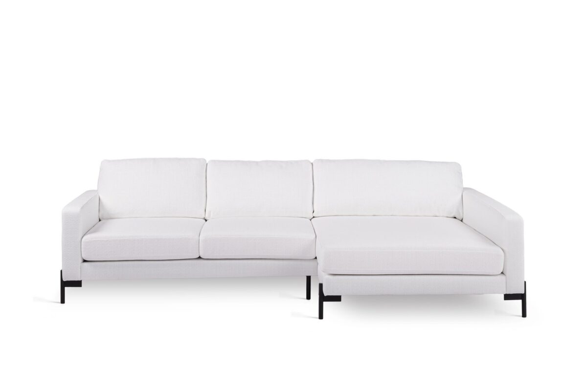 Een moderne witte sectionele bank met drie kussens en een chaise longue aan de rechterkant. Het heeft een strak design met armleuningen en wordt ondersteund door zwarte metalen poten, tegen een effen witte achtergrond.