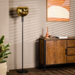 Een kamer met een houten kast, een hoge zwarte staande lamp met een gouden glazen kap en een plant. Aan de muur hangt een ingelijst abstract kunstwerk met gebogen vormen. De kamer heeft een warme, moderne esthetiek.