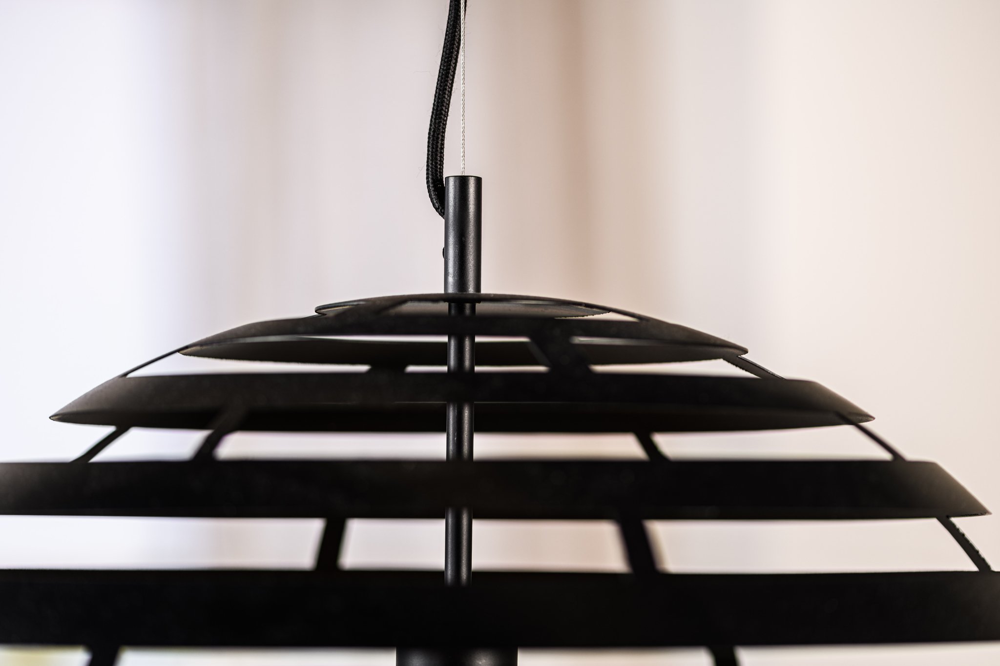 Close-up van een moderne zwarte hangende hanglamp met concentrische ronde metalen ringen, opgehangen aan een zwart snoer. De achtergrond is zacht vervaagd, wat een minimalistische en eigentijdse uitstraling creëert.