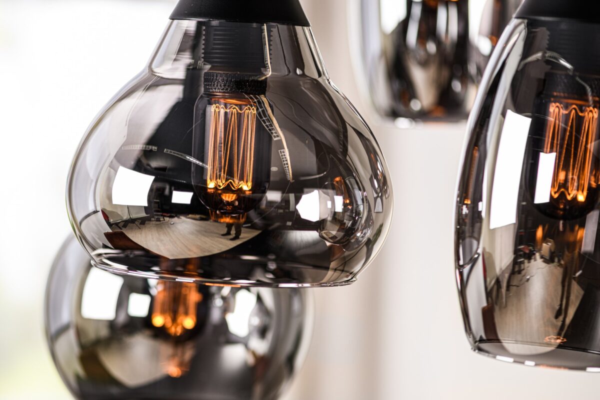 Close-up van moderne hanglampen met zichtbare gloeilampen. De lampen hebben reflecterende, rokerige glazen kappen die een warme gloed uitstralen. De achtergrond is zacht vervaagd, waardoor het ontwerp van de armaturen wordt benadrukt.