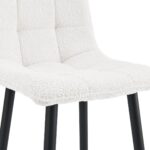 Close-up van een moderne stoel met een getextureerde witte stoffen zitting en zwarte metalen poten. Het ontwerp heeft een gewatteerd patroon op het gestoffeerde oppervlak, wat een minimalistische en eigentijdse stijl uitstraalt.