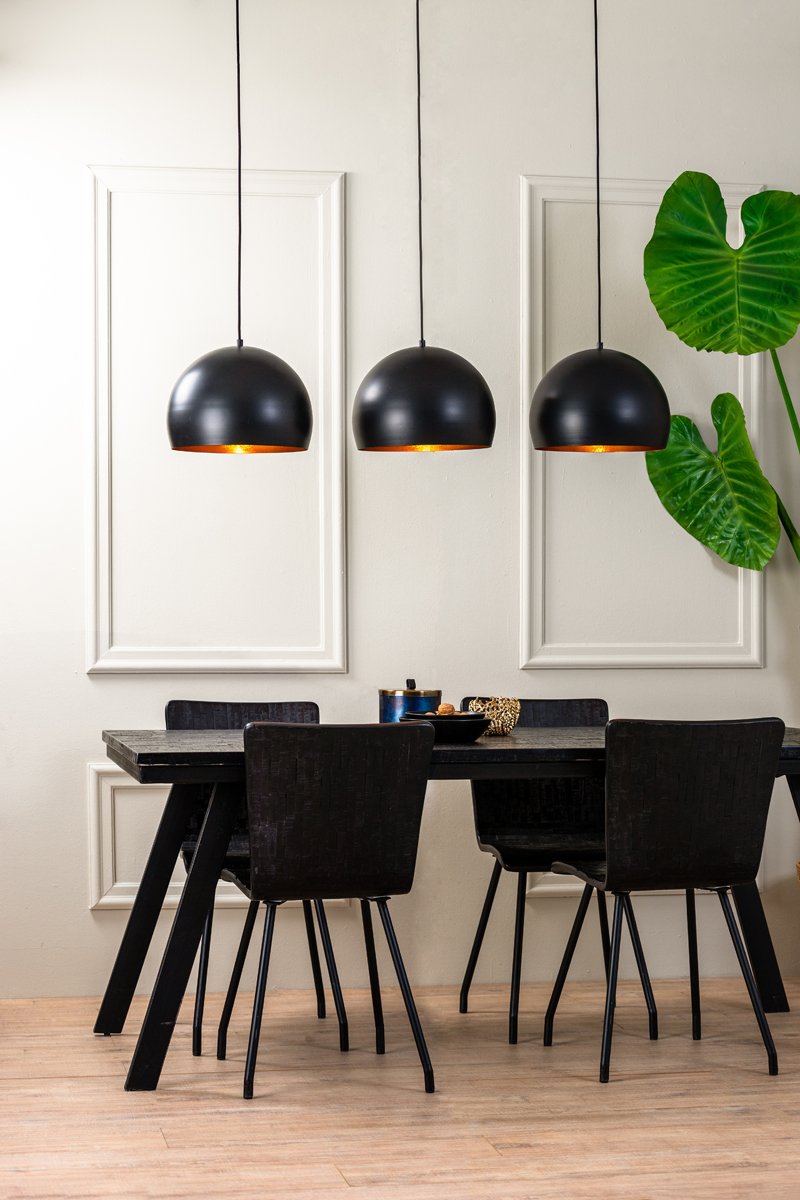 Een moderne eethoek met een zwarte tafel en vier stoelen. Boven de tafel hangen drie zwarte koepelvormige hanglampen. Een groot groen blad zorgt voor een vleugje kleur tegen de witte muur met decoratieve lijstwerk. Lichte houten vloer maakt de look compleet.