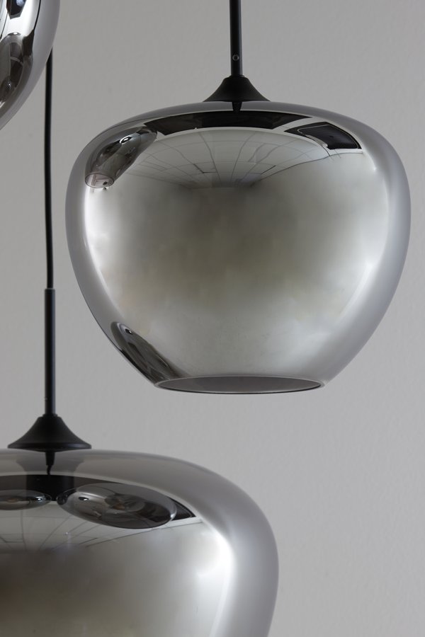 Close-up van twee moderne, metalen hanglampen met een reflecterend, zilverkleurig oppervlak. Het bovenste licht is gedeeltelijk zichtbaar, terwijl het onderste licht reflecties van een kamerinterieur op een grijze achtergrond laat zien.
