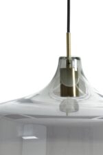 Close-up van een moderne hanglamp met een glazen kap en een goudkleurige metalen armatuur. De lamp hangt aan een zwart snoer tegen een witte achtergrond. Het glas heeft een strakke, glanzende afwerking die licht en omgeving reflecteert.