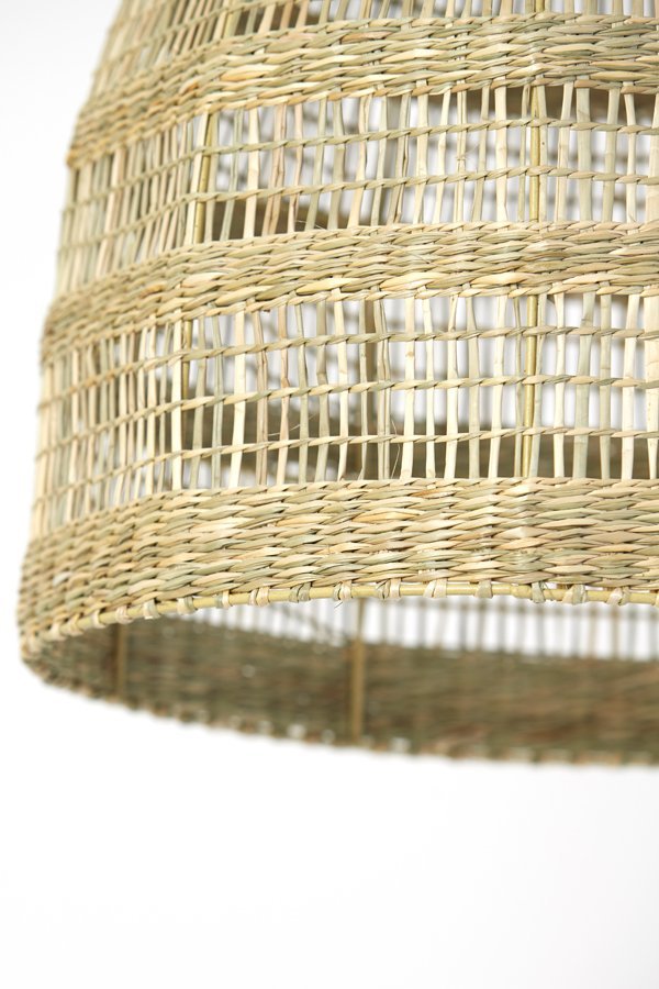 Close-up van een gevlochten rieten lampenkap met een natuurlijke afwerking. Het patroon bestaat uit een reeks horizontale en verticale weefsels, wat een gestructureerde en luchtige uitstraling creëert tegen een effen witte achtergrond.