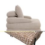 Een moderne, beige gestoffeerde fauteuil met gelaagde kussens. De stoel heeft een uniek ontwerp met verschillende texturen en een patroon in bruin en wit op het onderste deel. De stoel heeft strakke zwarte metalen poten.