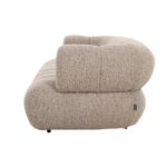 Zijaanzicht van een beige, getextureerde bank met afgeronde randen en pluche kussens. De stof lijkt zacht en het algehele ontwerp is modern en minimalistisch. Een klein zwart label is bevestigd aan het onderste deel van de bank.