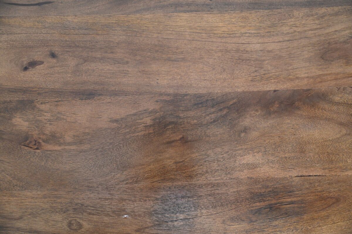 Houten oppervlak met een natuurlijke, rustieke textuur. De houtnerf is prominent aanwezig en vertoont een mix van lichte en donkerbruine tinten met een paar knopen en onvolkomenheden, wat het een aardse en organische uitstraling geeft.