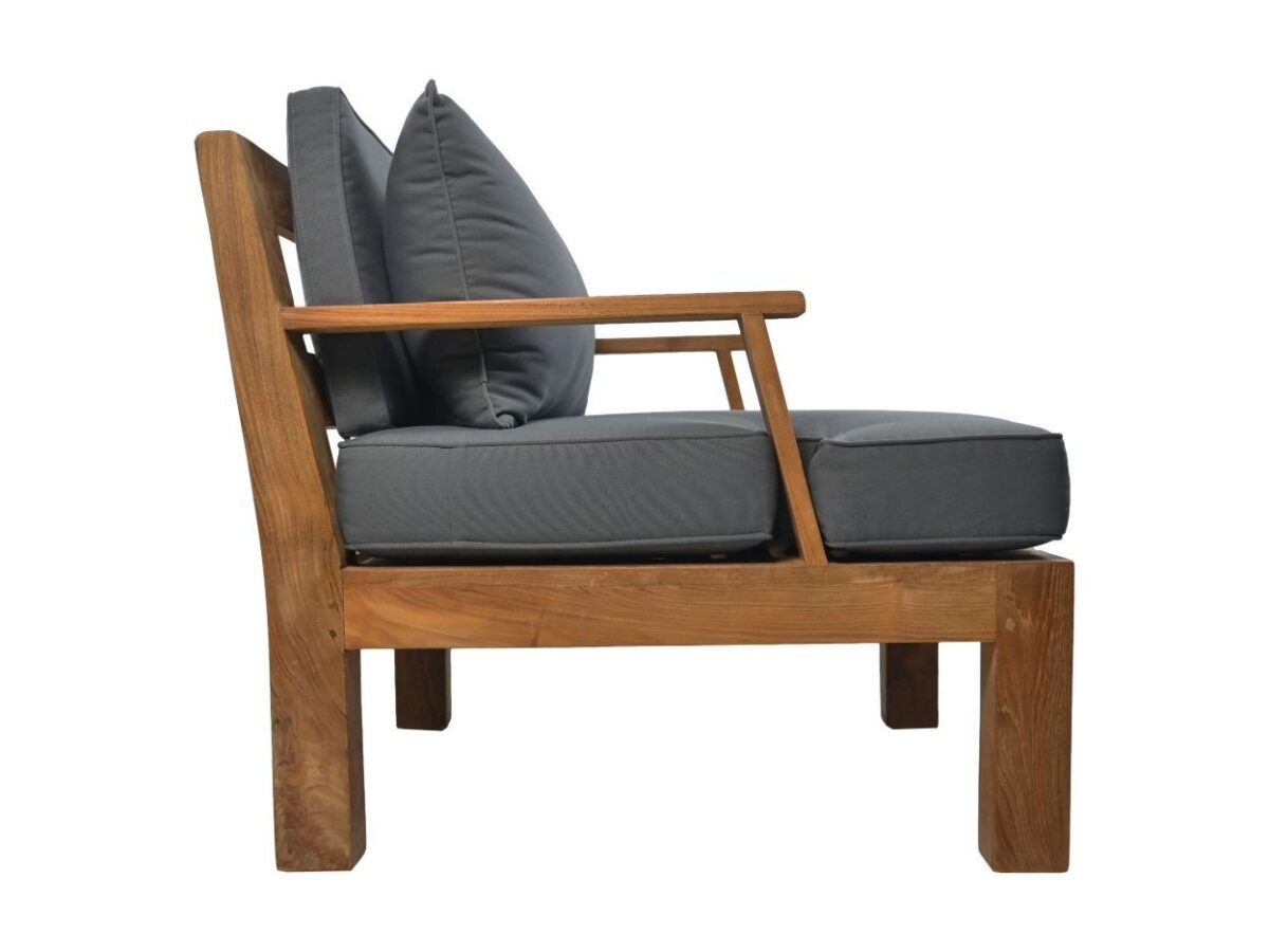 Zijaanzicht van een houten fauteuil met donkergrijze kussens en twee rugkussens. De stoel heeft een eenvoudig ontwerp met een schuine rugleuning en strakke lijnen. Het hout heeft een natuurlijke afwerking.