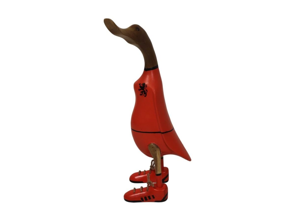 Een houten eend, oranje geverfd, rechtopstaand. Hij draagt oranje laarzen met zwarte details en een zwart leeuwenembleem op zijn borst. De eend heeft een natuurlijke houtkleur voor de kop en snavel.