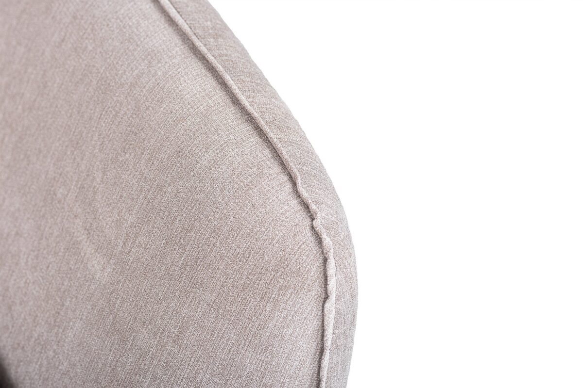 Close-up van de hoek van een beige stoffen bank met zichtbare stiksels. De textuur van de bekleding en het naaddetail zijn prominent aanwezig tegen een witte achtergrond.