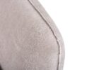 Close-up van de hoek van een beige stoffen bank met zichtbare stiksels. De textuur van de bekleding en het naaddetail zijn prominent aanwezig tegen een witte achtergrond.