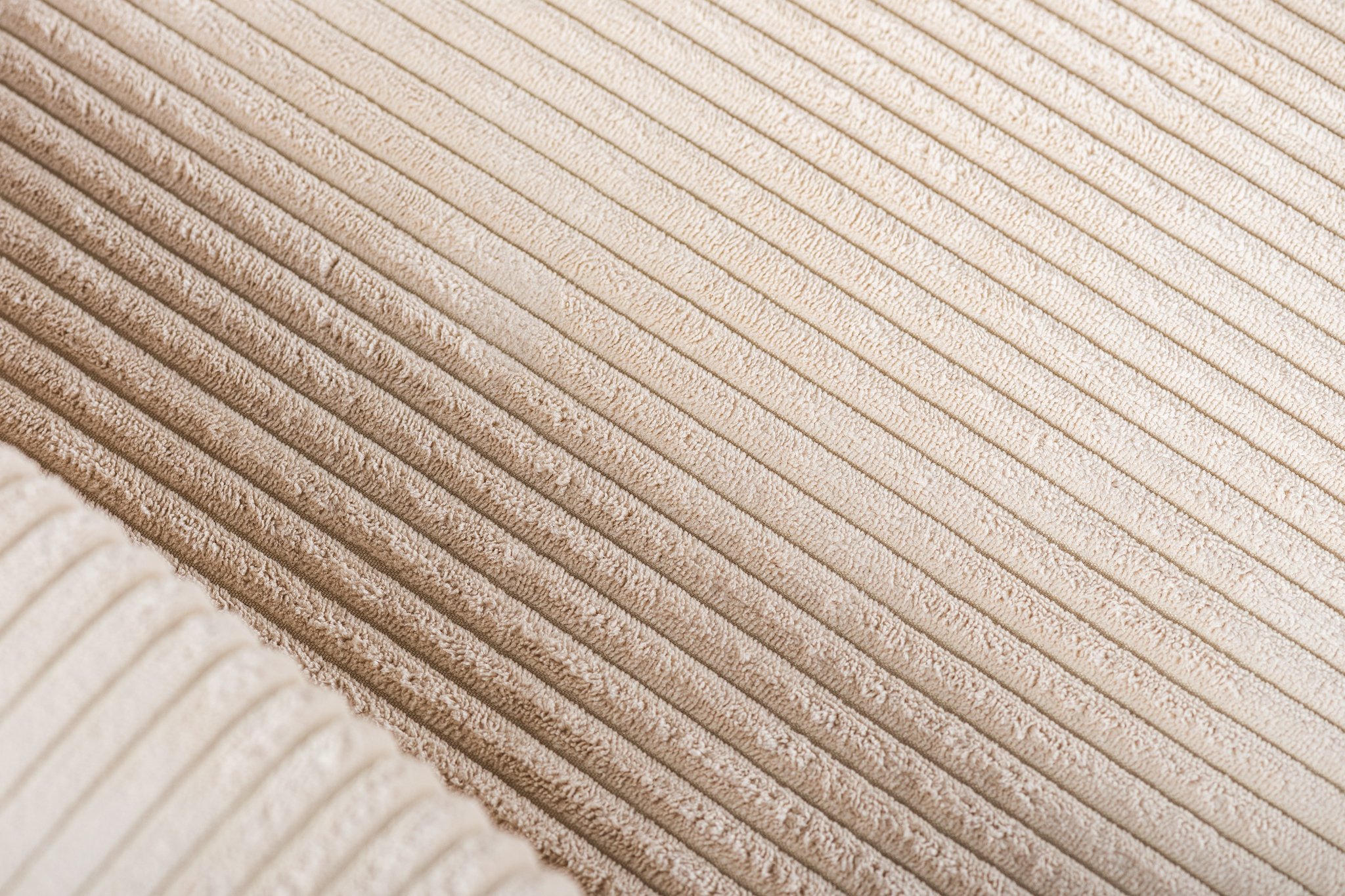 Close-up van een beige corduroystof met het zachte, gestructureerde oppervlak met parallelle, verticale ribbels. De stof heeft een warme uitstraling en benadrukt het kenmerkende patroon dat kenmerkend is voor corduroymateriaal.