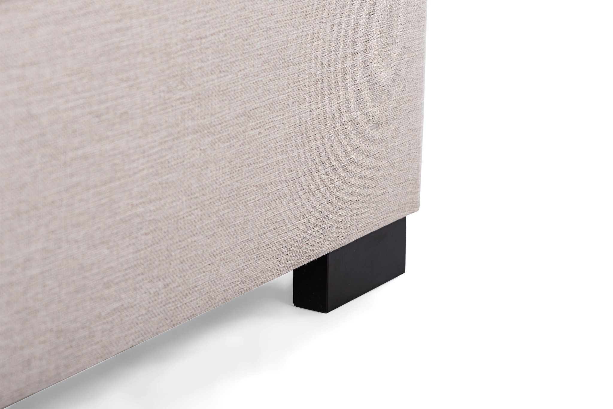 Close-up van een beige stoffen hoekbank met het getextureerde materiaal en de donkere houten poot op een witte achtergrond. De afbeelding richt zich op de constructie en ontwerpdetails van de bank.