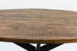 Een rond houten tafelblad met een gladde afwerking en zichtbare nerfpatronen. De tafel heeft een natuurlijke bruine kleur en wordt ondersteund door een zwarte metalen basis. De achtergrond is een lichte, neutrale kleur.