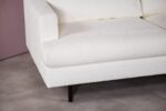 Close-up van een witte, getextureerde bank met strakke lijnen en zwarte poten, tegen een neutrale tegelvloer en een lichtgekleurde muur.