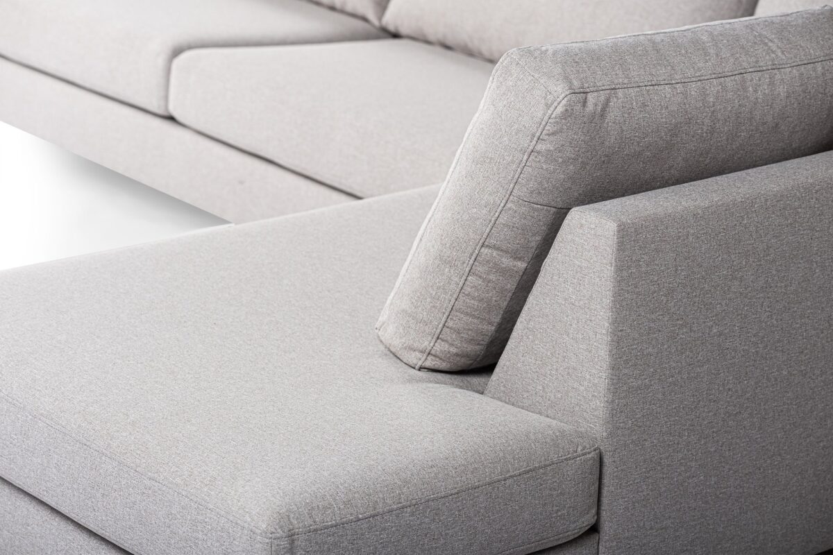 Close-up van een moderne grijze stoffen bank met een hoekige rugleuning en zachte kussens. Het sectionele stuk heeft strakke lijnen en een minimalistisch design, wat de eigentijdse stijl en het comfort benadrukt.