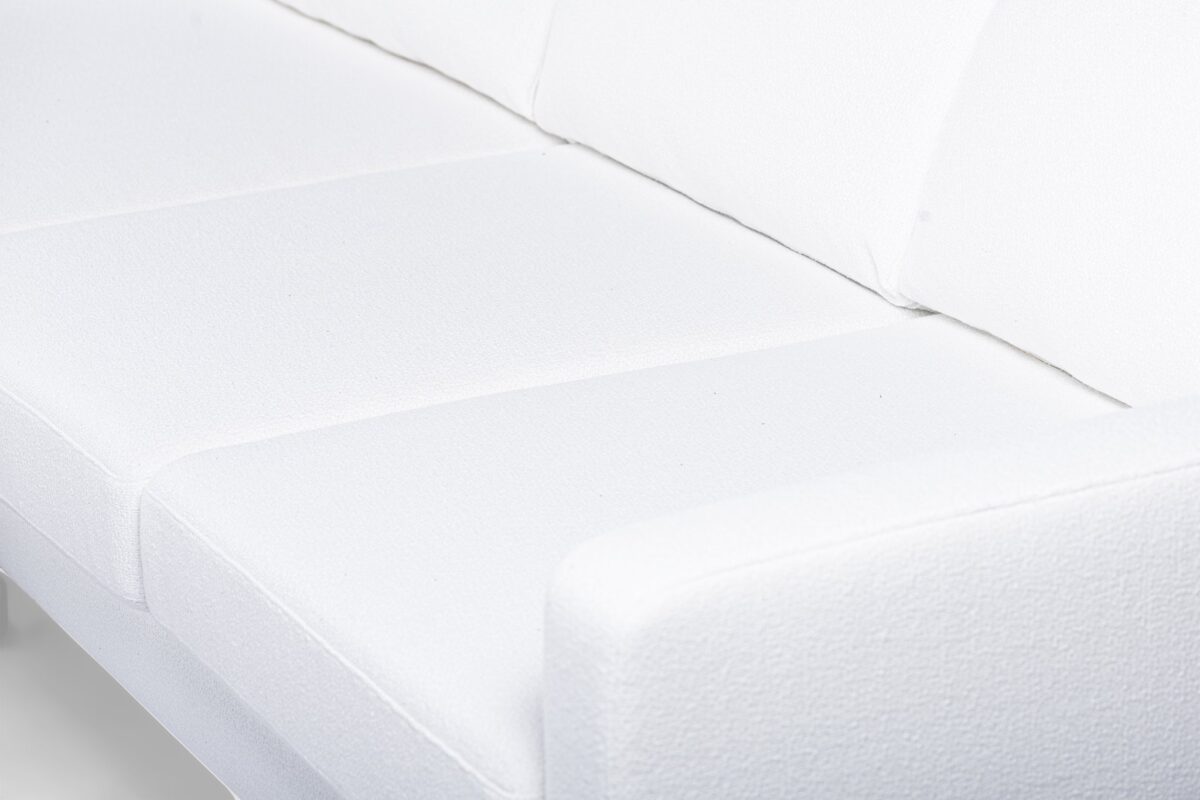 Close-up van een witte, moderne bank met een minimalistisch design. De afbeelding richt zich op drie zitkussens en de armleuning aan de rechterkant, waardoor de strakke lijnen en textuur van de bank worden benadrukt.