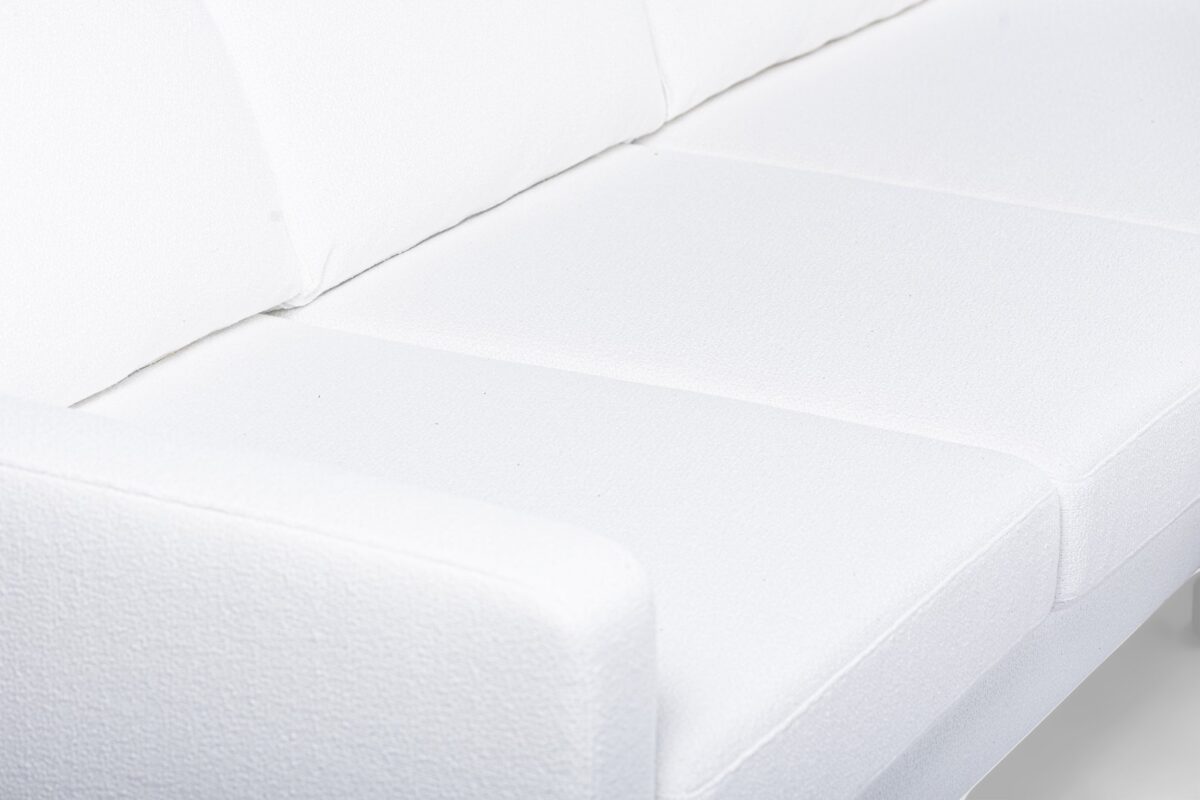 Een close-up van een witte gestoffeerde bank met een modern design. De afbeelding richt zich op de strakke lijnen en zachte textuur van de stof die de kussens en armleuningen bedekt.