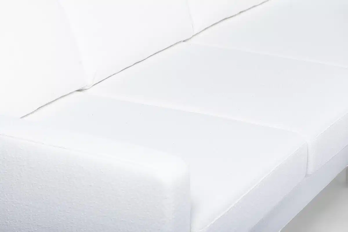 Een close-up van een witte gestoffeerde bank met een modern design. De afbeelding richt zich op de strakke lijnen en zachte textuur van de stof die de kussens en armleuningen bedekt.