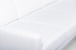 Een close-up van een witte gestoffeerde bank met een modern design. De afbeelding richt zich op de strakke lijnen en zachte textuur van de stof die de kussens en armleuningen bedekt.
