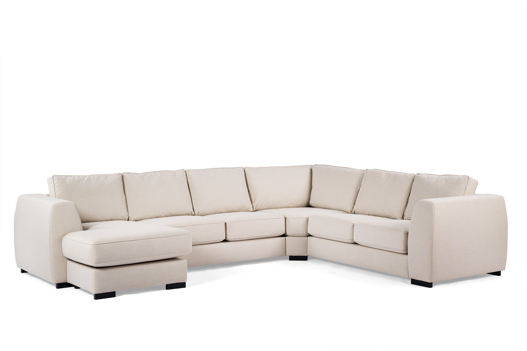 Een grote beige sectionele bank met een chaise longue aan de linkerkant, tegen een effen witte achtergrond. De bank heeft zes gewatteerde rugleuningen en armleuningen aan beide uiteinden, allemaal ondersteund door donkere houten poten.