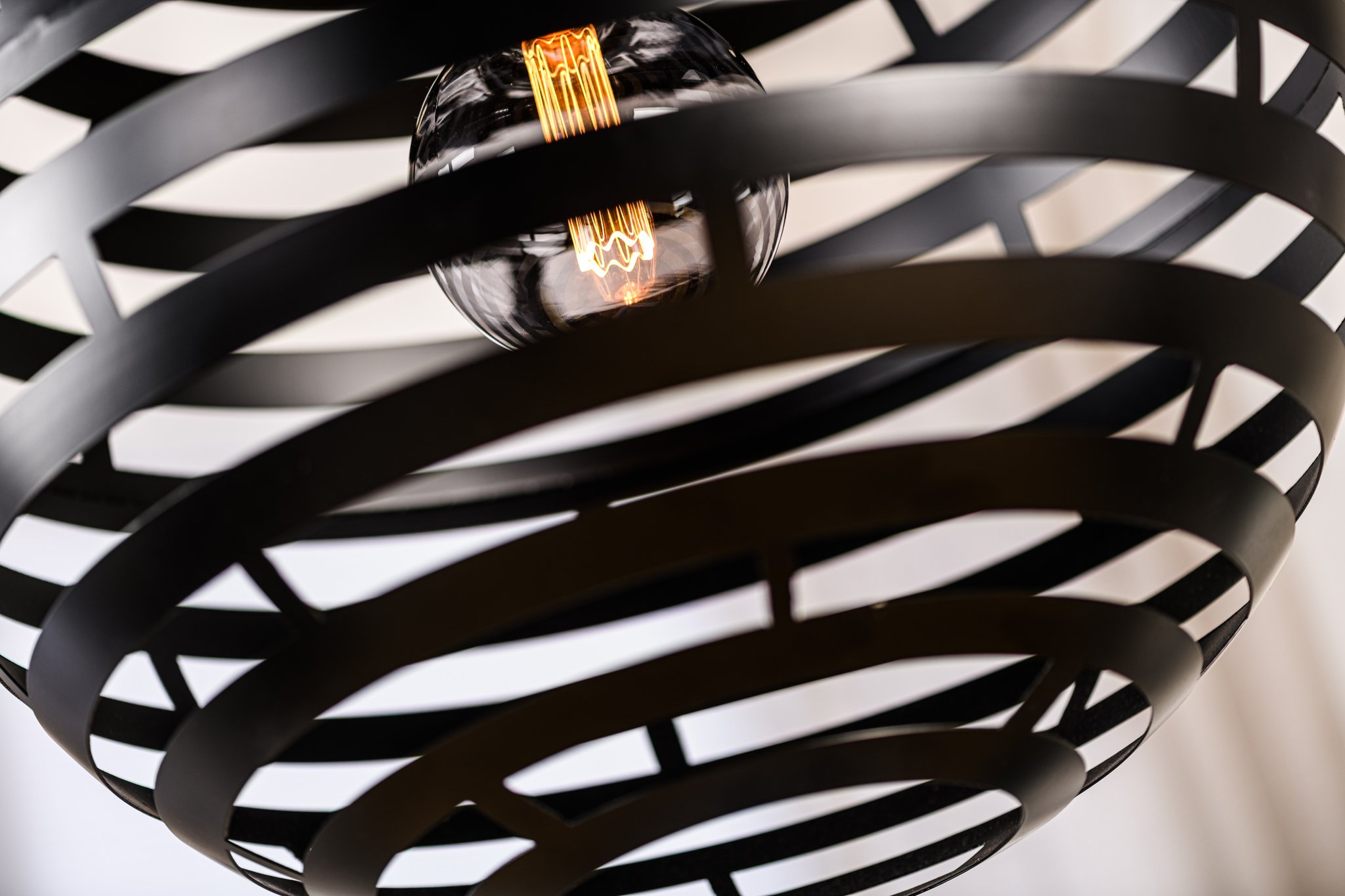 Close-up van een moderne lamp met een zwart geometrisch spiraalvormig ontwerp. Een gloeiende gloeilamp is zichtbaar in het midden, die warm licht werpt door de open ruimtes van het spiraalpatroon.