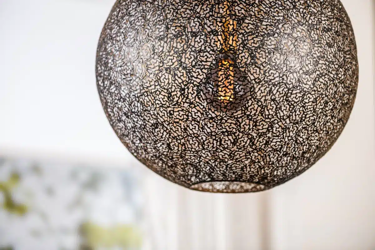 Close-up van een bolvormige hanglamp met een ingewikkeld zwart kantpatroon dat een gloeiende lamp binnenin onthult. De achtergrond is zacht vervaagd, waardoor het gedetailleerde ontwerp van de lamp wordt benadrukt.