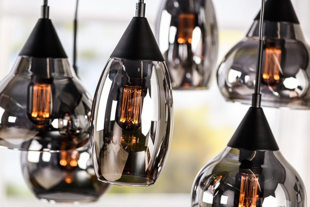 Close-up van moderne hangende hanglampen met strakke glazen kappen en zichtbare gloeilampen. De gloeilampen stralen een warme gloed uit, die weerkaatst op de gepolijste oppervlakken, waardoor een stijlvolle en eigentijdse ambiance ontstaat.