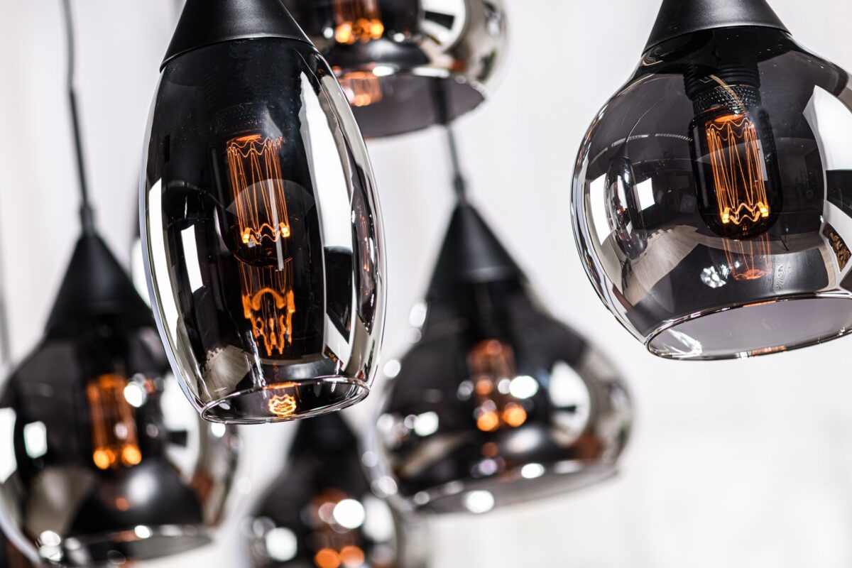 Close-up van verschillende hangende hanglampen met zwarte armaturen en transparante, reflecterende glazen kappen. De warme amberkleurige gloed van de verlichte gloeilampen binnenin creëert een gezellige ambiance.