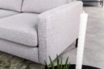 Close-up van de 3 zits bank CL L+R in Valente V311 grijs stof met vierkante armleuning, getoond met een groen vloerkleed, plant en witte structuurkaars op een zwarte ronde tafel. De setting heeft een lichtgekleurde tegelvloer.