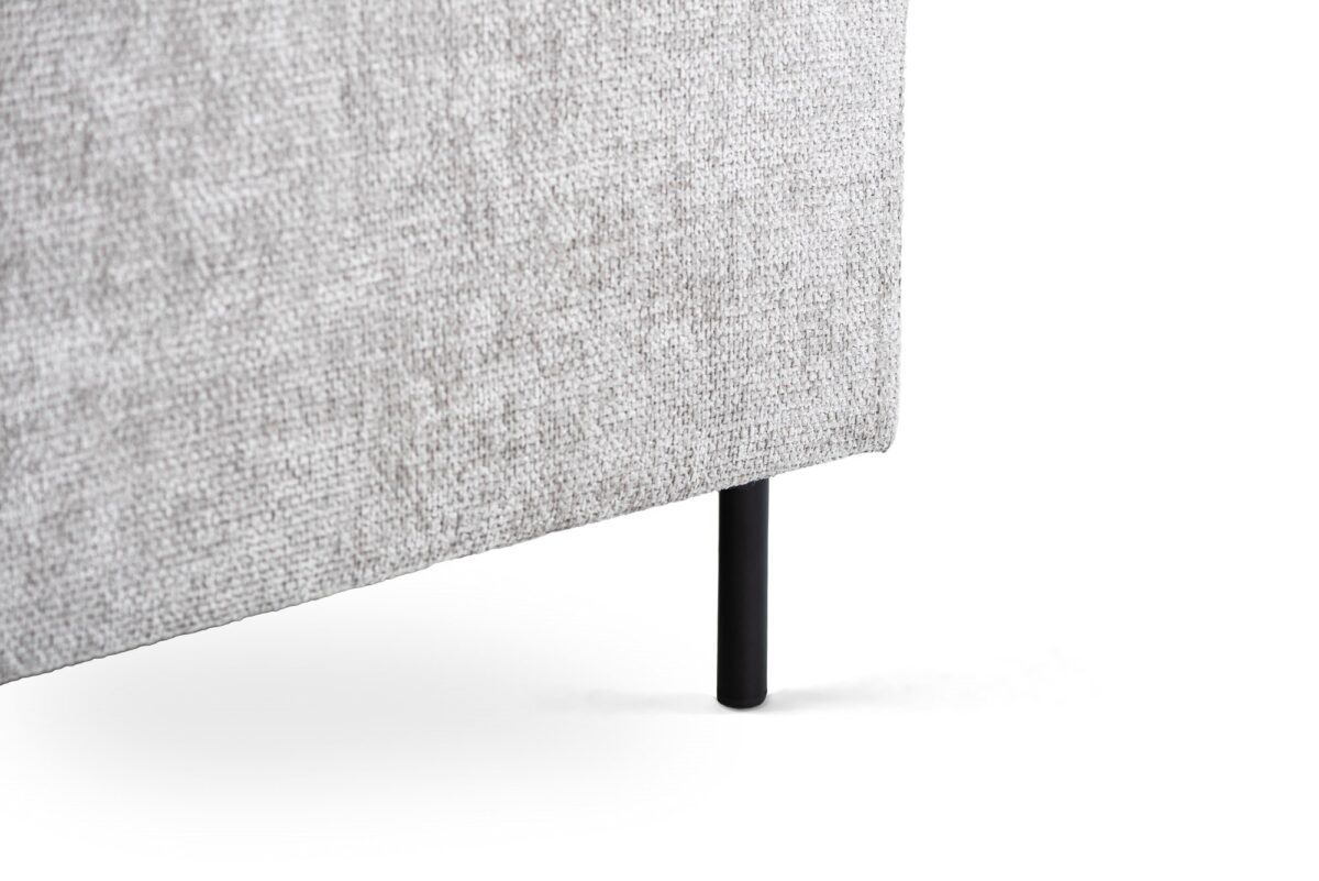 Close-up van de onderste hoek van de 3 zits hoek links, stof Haga 08, E920 naturel met de lichtgrijze structuurstof en enkele zwarte metalen cilindervormige poot tegen een witte achtergrond.