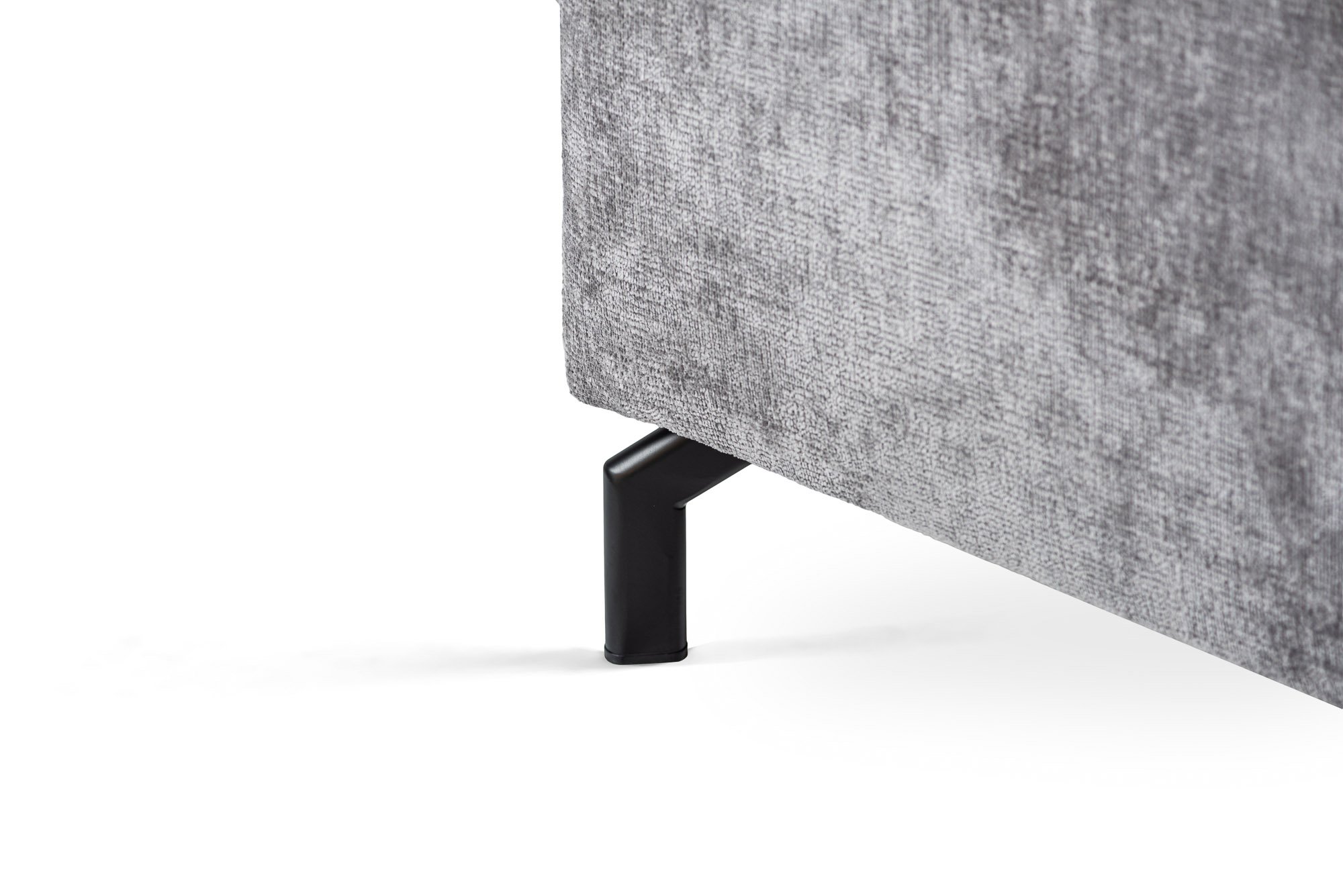 Close-up van een grijs stoffen meubel met een metalen poot. De textuur van de stof is zichtbaar zacht en licht glanzend. De metalen poot is zwart en heeft een modern, hoekig design. De achtergrond is effen wit.