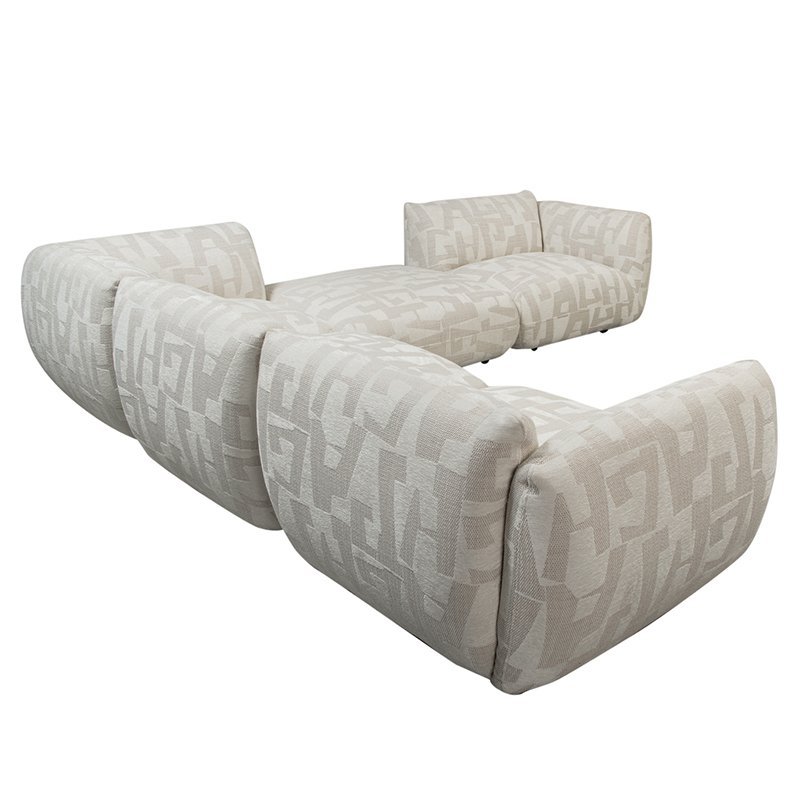 Een beige modulaire bank met een geometrisch patroon, met vier grote kussens die een L-vorm vormen. De stof heeft een subtiel, abstract lineair ontwerp en de bank oogt pluche en uitnodigend.