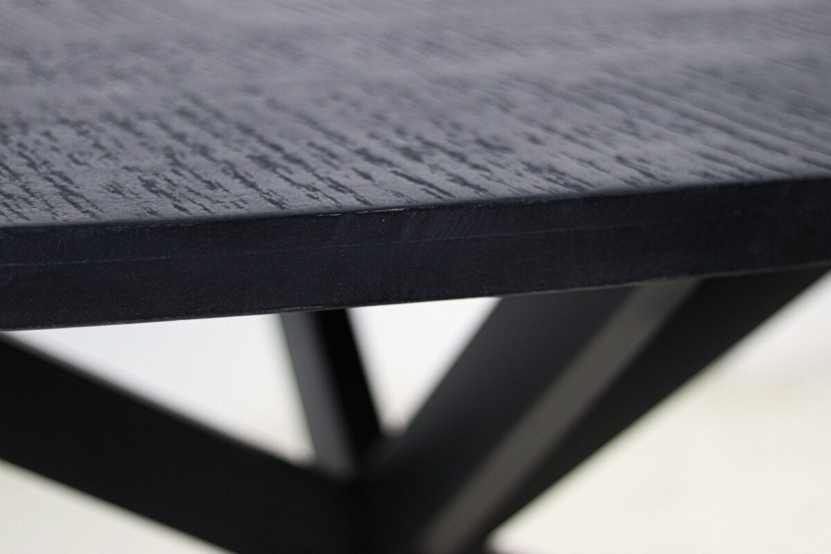Close-up van een donkergekleurde houten tafel met een glad, gestructureerd oppervlak. De rand van het tafelblad is scherp, terwijl de achtergrond een wazig kruislings basisontwerp laat zien.