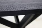 Close-up van een donkergekleurde houten tafel met een glad, gestructureerd oppervlak. De rand van het tafelblad is scherp, terwijl de achtergrond een wazig kruislings basisontwerp laat zien.