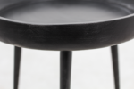 Close-up van een zwarte houten tafel met slanke poten. De tafel heeft een rond blad en een glad, licht getextureerd oppervlak. De achtergrond is zacht vervaagd, wat het minimalistische ontwerp van de tafel benadrukt.