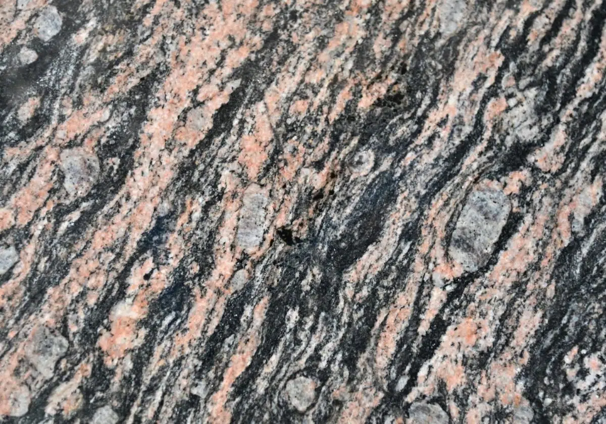 Close-up van een gepolijst granieten oppervlak met wervelende patronen van roze en donkergrijs. De textuur toont kleine, ronde minerale insluitsels die een ingewikkeld, natuurlijk ontwerp creëren.