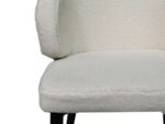 Close-up van een witte, getextureerde, gebogen rugleuning met zwarte poten. De bekleding lijkt zacht en pluche, met een focus op de zitting en een deel van de rugleuning.