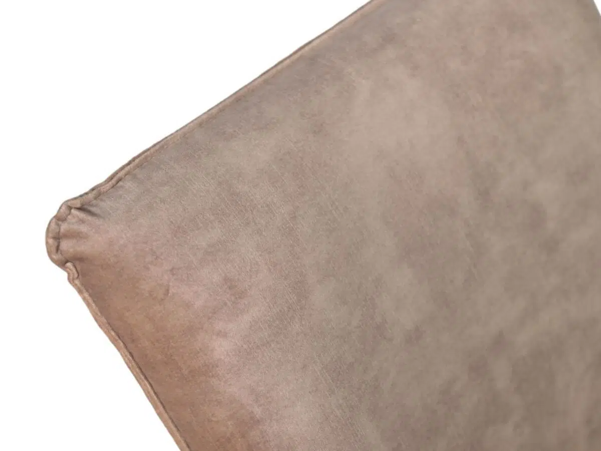Close-up van een beige suède kussen met een zachte textuur. Het kussen is schuin geplaatst, waardoor de bovenste hoek en zijkant zichtbaar zijn. De stof lijkt glad, met zichtbare naden langs de randen.