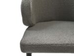 Close-up van een grijze, getextureerde fauteuil met een gebogen rugleuning. De stof lijkt zacht en heeft een bouclé-textuur. De stoel heeft metalen poten, gedeeltelijk zichtbaar aan de onderkant.