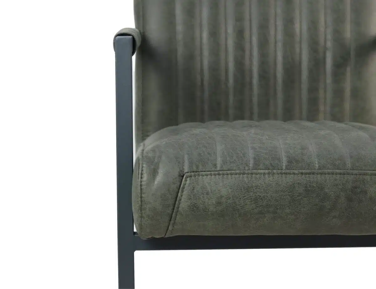 Close-up van een stoel met donkergroene, verticaal gestikte bekleding. De stoel heeft een zwart metalen frame en armleuning, wat een modern design laat zien. De textuur van de stof is zichtbaar, wat het een licht verweerde uitstraling geeft.