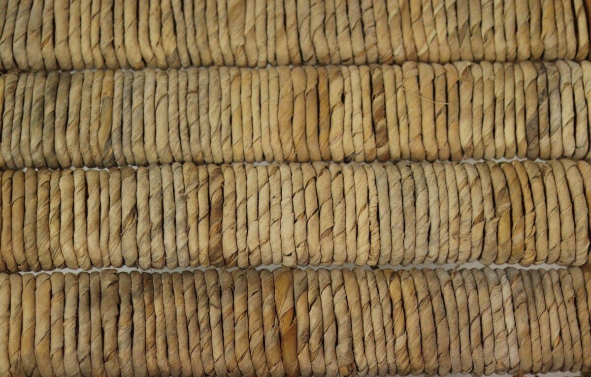 Close-up van strak geweven strotouwen gerangschikt in parallelle rijen, waardoor een getextureerd patroon ontstaat. De natuurlijke vezels variëren in tinten beige en lichtbruin, wat een rustieke en handgemaakte uitstraling geeft.