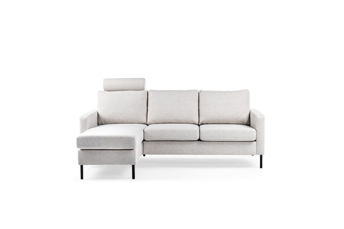 Een moderne, lichtgrijze sectionele bank met drie kussens en een chaise longue aan de linkerkant. Het heeft strakke, zwarte poten en een afneembare hoofdsteun op de linkerzitting, tegen een effen witte achtergrond.